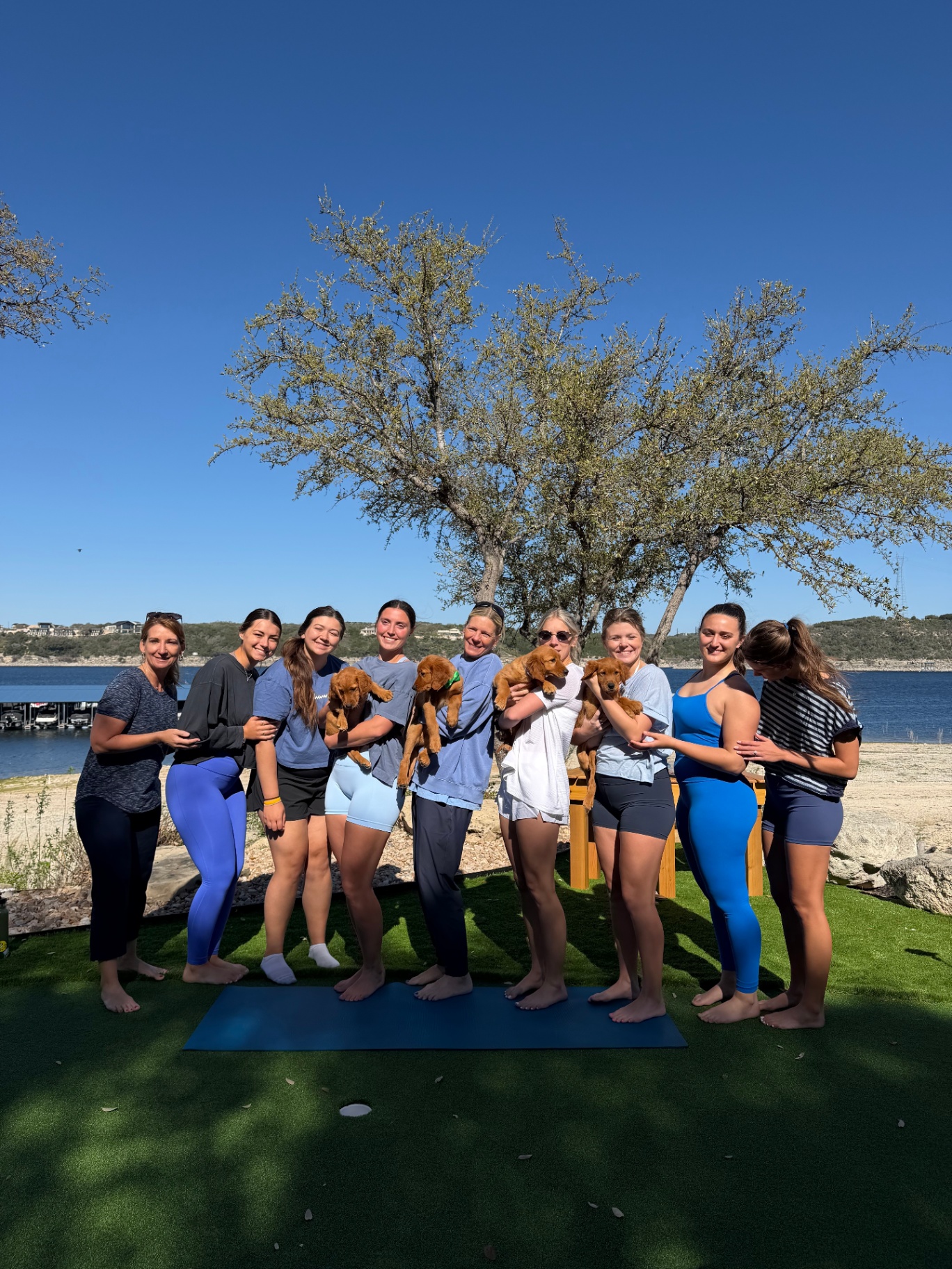 Group of puppy yoga guests posing by the lake with puppies