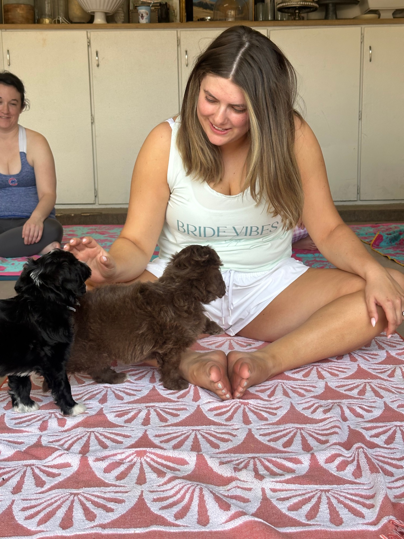 Bride-to-be in a Bride Vibes tank top playing with two tiny puppies during a bachelorette class