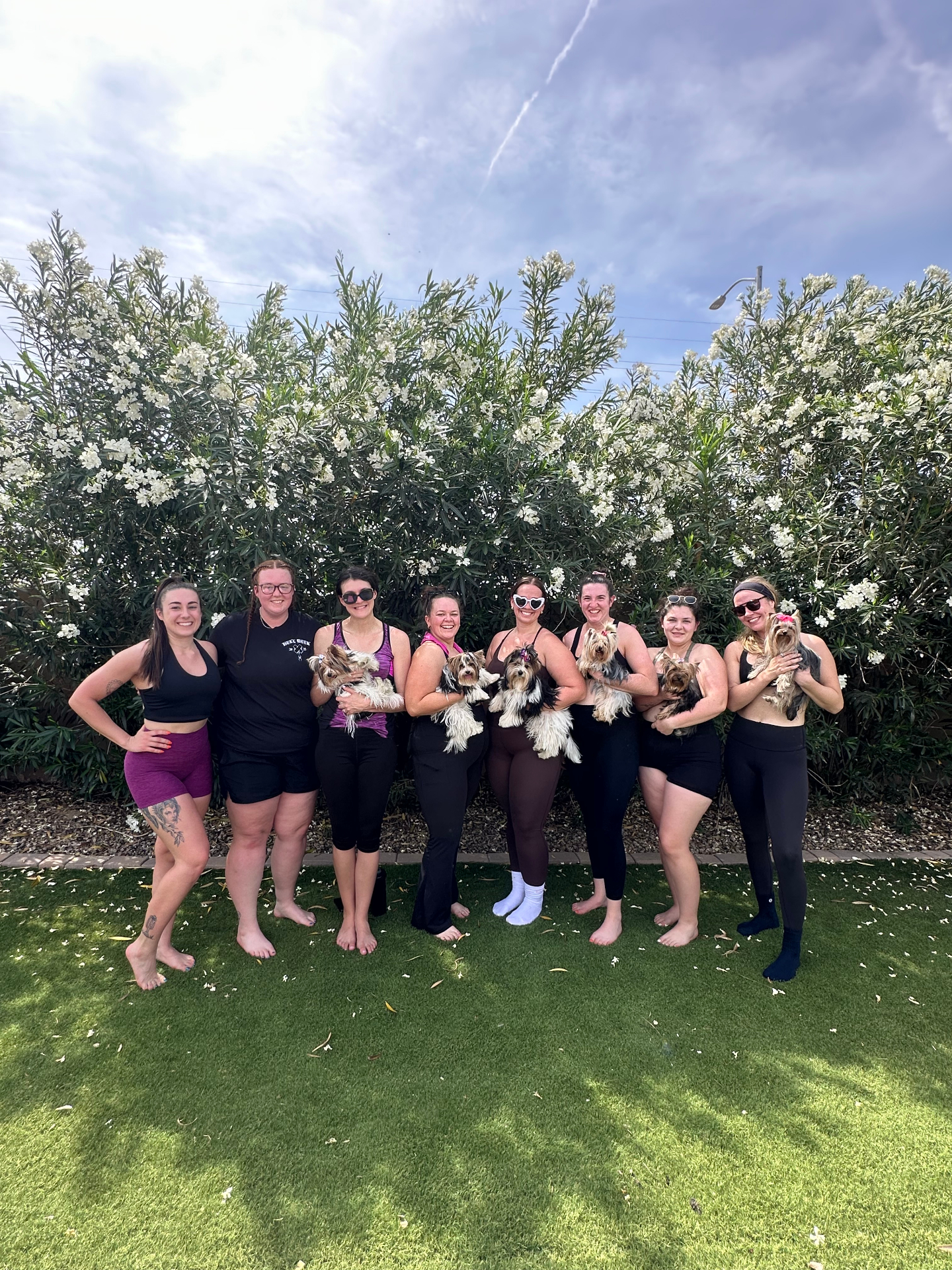 Scottsdale group standing in front of flowering hedges holding yorkies after class